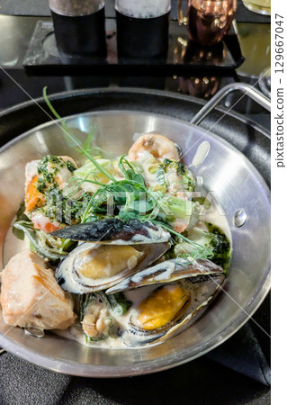 Hot pan with seafood. Mussels, squid, shrimp, salmon, zucchini in creamy sauce 129667047