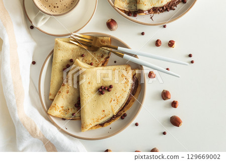 Crepes with chocolate hazelnut spread, strawberries and hazelnuts on a white wooden table. Top view 129669002