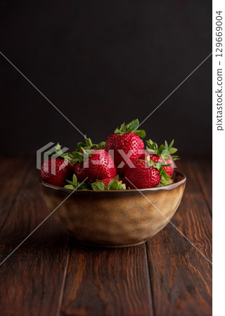 Fresh red strawberries in a rustic bowl on a dark wooden background. Front view Fresh red strawberries in a rustic bowl on a dark wooden background. Front view 129669004