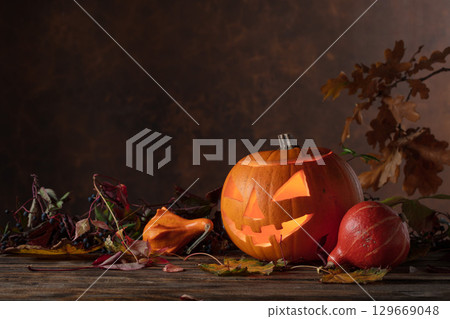 Halloween pumpkin head jack lantern with dried-up leaves. Halloween pumpkin head jack lantern with dried-up leaves. 129669048