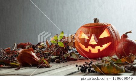 Halloween pumpkin head jack lantern with dried-up leaves. Halloween pumpkin head jack lantern with dried-up leaves. 129669049