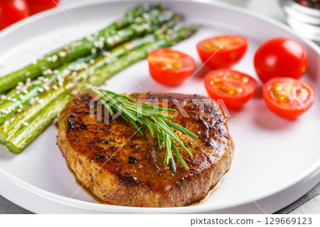 Grilled beef steak closeup with asparagus and cherry tomatoes on white plate, gourmet healthy dinner 129669123