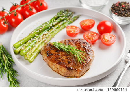 Grilled beef steak closeup with asparagus and cherry tomatoes on white plate, gourmet healthy dinner 129669124
