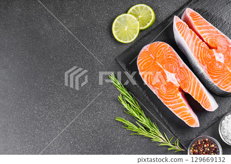 Fresh raw salmon or trout steaks with tomatoes, spices, rosemary and lime on black stone background 129669132