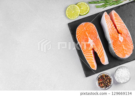 Two fresh raw salmon steaks with tomatoes, spices, rosemary and lime on white stone background 129669134
