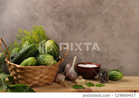 Fresh cucumbers in basket, spices, garlic and leaves on concrete table, village harvest, homemade pickling recipe, cucumbers and pickling ingredients, home canning concept, healthy and natural food 129669457