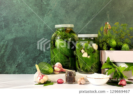 Pickled cucumbers in a jar with garlic and dill on the kitchen table, village harvest, homemade pickling recipe, cucumbers and ingredients for pickling, home canning concept, healthy and natural food. 129669467