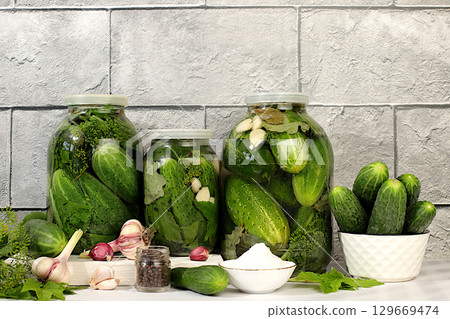 Pickled cucumbers in jars with garlic and dill on wooden kitchen table, rustic style,Homemade pickling recipe, cucumbers and ingredients for pickling, home canning concept 129669474