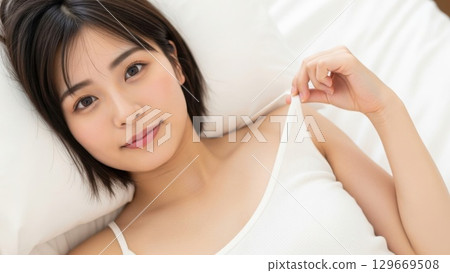 A woman lying on the bed and touching the shoulder straps of her camisole 129669508