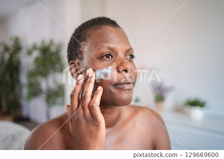 Mid adult woman moisturizing her face with cream 129669600
