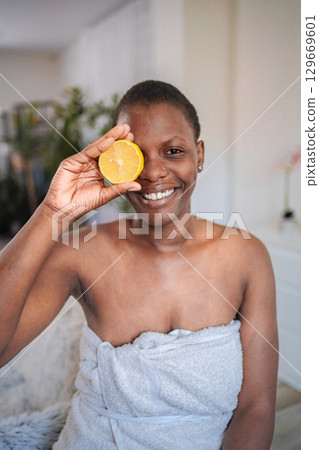 Young woman holding a lemon slice in front of her eye and smiling Young woman holding a lemon slice in front of her eye and smiling 129669601