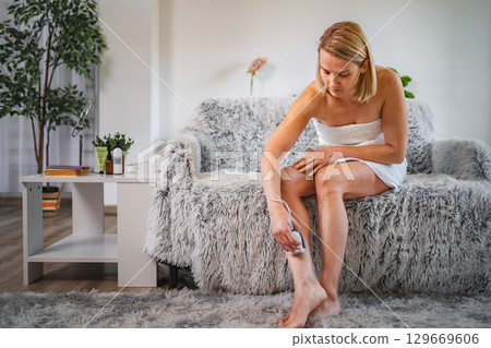 Woman removing leg hair with an electric epilator at home Woman removing leg hair with an electric epilator at home 129669606