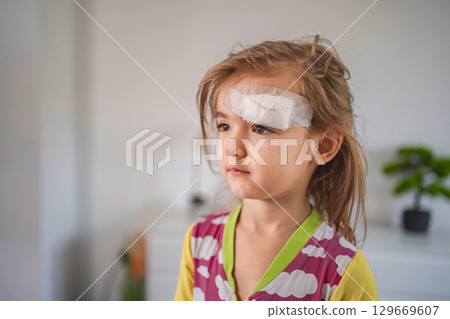 Little girl with band aid on forehead recovering from domestic accident Little girl with band aid on forehead recovering from domestic accident 129669607