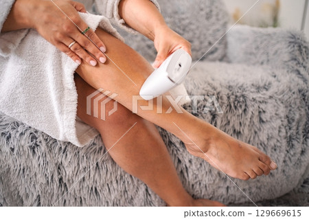 Woman removing leg hair with an electric epilator at home Woman removing leg hair with an electric epilator at home 129669615