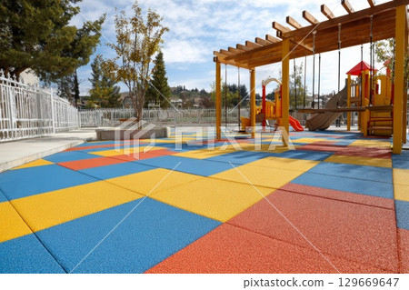 Colorful rubber flooring in a playground area with swings and climbing structures for children 129669647