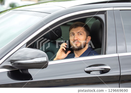 Man making a phone call while parked in a black car on a bright day 129669690