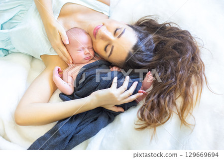Mother cherishes newborn baby during peaceful moment at home in soft bedding Mother cherishes newborn baby during peaceful moment at home in soft bedding 129669694