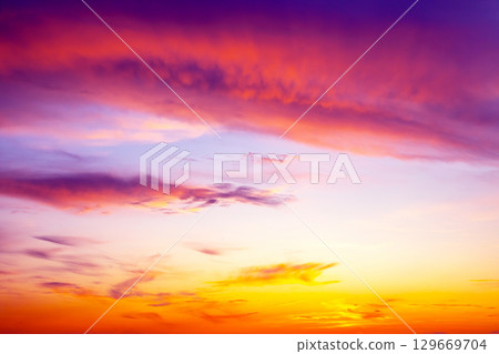 Vibrant sunset fills the sky with hues of orange, purple, and pink over a tranquil horizon 129669704