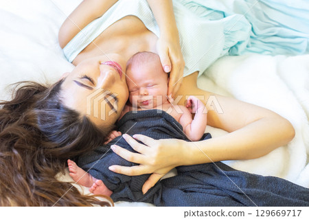 New mother cuddles her newborn baby on soft blanket in cozy indoor setting 129669717
