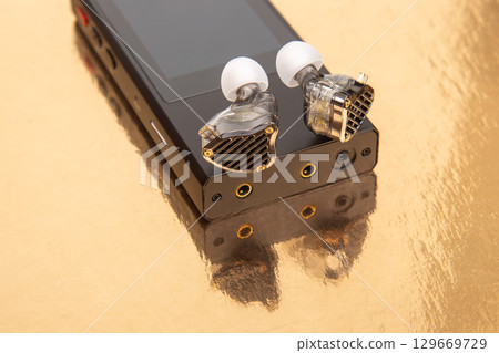 High-quality audio gear showcasing custom earphones on reflective gold surface 129669729
