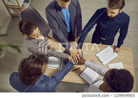 Determined to succeed, businesspeople fold their hands on top of each other in office. Determined to succeed, businesspeople fold their hands on top of each other in office. 129669983