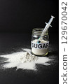 Jar of sugar with syringe on black background highlighting harmful effects of sugar consumption 129670042