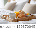 Breakfast tray with coffee, orange juice, croissant, and fresh fruit on a cozy bed 129670045