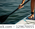 Close-up of paddleboarder gripping paddle with water droplets in serene lake environment 129670055
