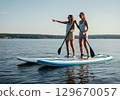 Two women paddleboarding on a calm lake, enjoying the sunny day and sharing laughter together 129670057