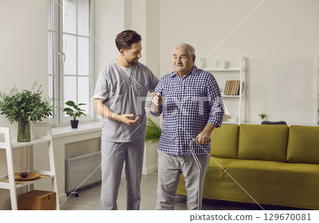 Young nurse man helping a senior patient to walk with his crutches. 129670081