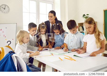 Group of elementary school students completes task together with young female teacher. Group of elementary school students completes task together with young female teacher. 129670088