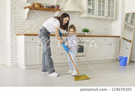Smiling mother with cute daughter sweeping floor with broom in kitchen at home. Smiling mother with cute daughter sweeping floor with broom in kitchen at home. 129670105