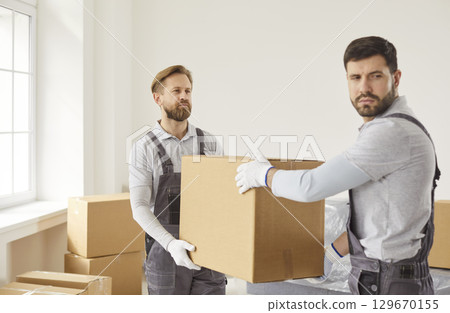 Two movers carrying cardboard boxes from clients house, unload items, dressed in overalls Two movers carrying cardboard boxes from clients house, unload items, dressed in overalls 129670155