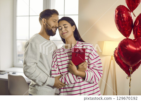 Man congratulating woman on holiday with red present box. Happy couple hugging in love. 129670192