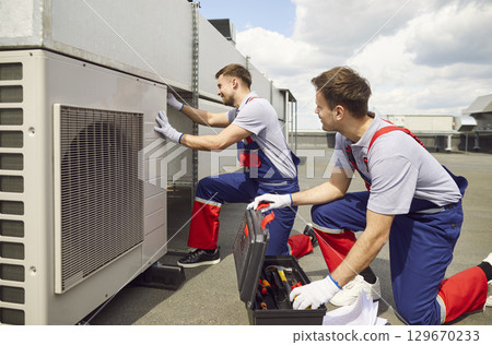 Team Of Engineers And Electricians Repairing Air Conditioning System On Roof 129670233