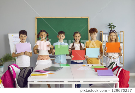 Positive elementary school teens boys and girls in casual clothes show colored paper sheets 129670237