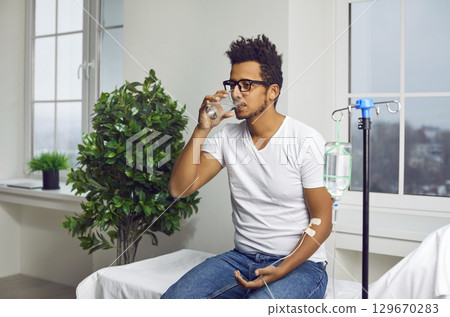Young man drinks water while receiving vitamin therapy through IV drip line infusion Young man drinks water while receiving vitamin therapy through IV drip line infusion 129670283