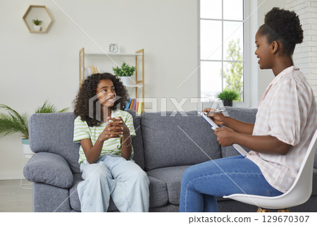 Happy African American girl sitting on couch and talking to her therapist or psychologist 129670307