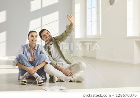 In spacious room, couple sits comfortably on floor and discusses layout of their new home. 129670376