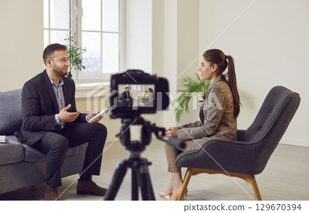 Digital camera on tripod recording interview of man and woman sitting and talking in TV show studio. 129670394