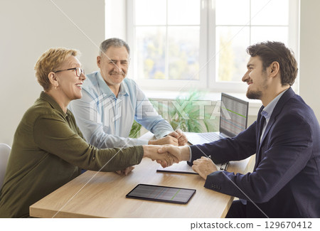 Smiling mature couple shaking hands with business consultant during financial planning meeting. 129670412