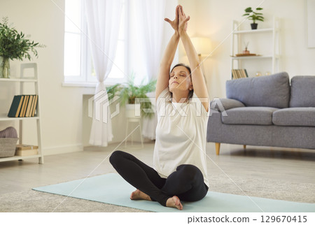 Senior woman in yoga lotus pose at home, learning basic poses, breathing techniques, practice 129670415