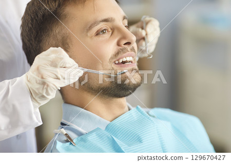 Young happy smiling male patient lying in modern dentistry clinic during medical check up. 129670427