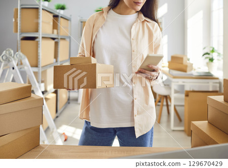 Internet store owner or inventory manager preparing parcels and using mobile phone Internet store owner or inventory manager preparing parcels and using mobile phone 129670429