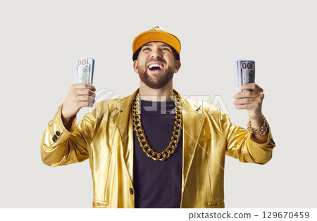 Funny young man in golden suit holding money cash on white studio background. 129670459