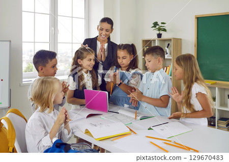 Happy multiethnic children with woman teacher have good time at school stand around classroom table Happy multiethnic children with woman teacher have good time at school stand around classroom table 129670483