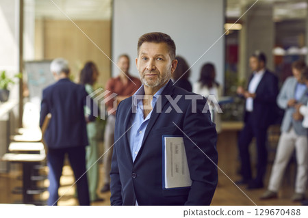 Confident mature business man looking at the camera standing in the office. Confident mature business man looking at the camera standing in the office. 129670488
