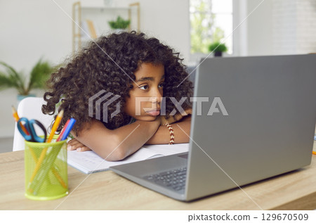 Bored schoolgirl without enthusiasm and interest watching online lesson on laptop at home. 129670509