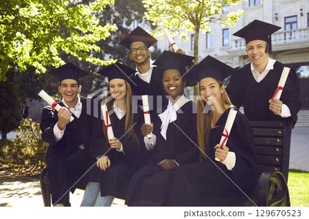 Happy group of multiracial people in graduation gowns with diplomas posing for group photo. Happy group of multiracial people in graduation gowns with diplomas posing for group photo. 129670523