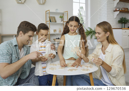 Cheerful young family with two children is having fun putting together wooden puzzles. 129670536